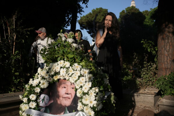A mourner pays her respects beside a floral wreath bearing a portrait of Kozo Okamoto, a former member of the Japanese Red Army militant group who died Thursday at age 78, at his grave during his burial at Martyrs' Cemetery in Beirut, Lebanon, Friday, July 24, 2026. (AP Photo/Hassan Ammar)