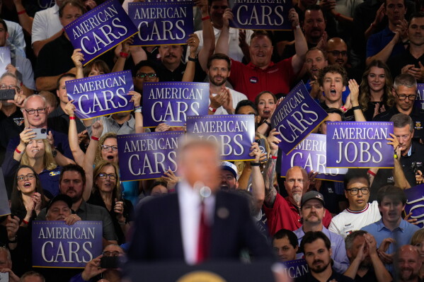 Attendees hold signs as President Donald Trump speaks at the General Motors Proving Ground, Monday, July 27, 2026, in Milford, Mich. (AP Photo/Paul Sancya)