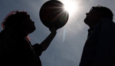 Silhouettes of two people with one person on the left holding up a circular object to block the sun, mimicking a solar eclipse.