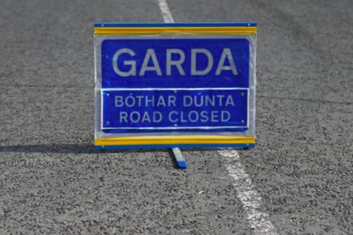 A Garda road closure sign is positioned on the side of the road, indicating that the path ahead is temporarily inaccessible due to official instructions. The sign is prominently displayed in blue and yellow with the text "GARDA ROAD CLOSED" in white letters.
