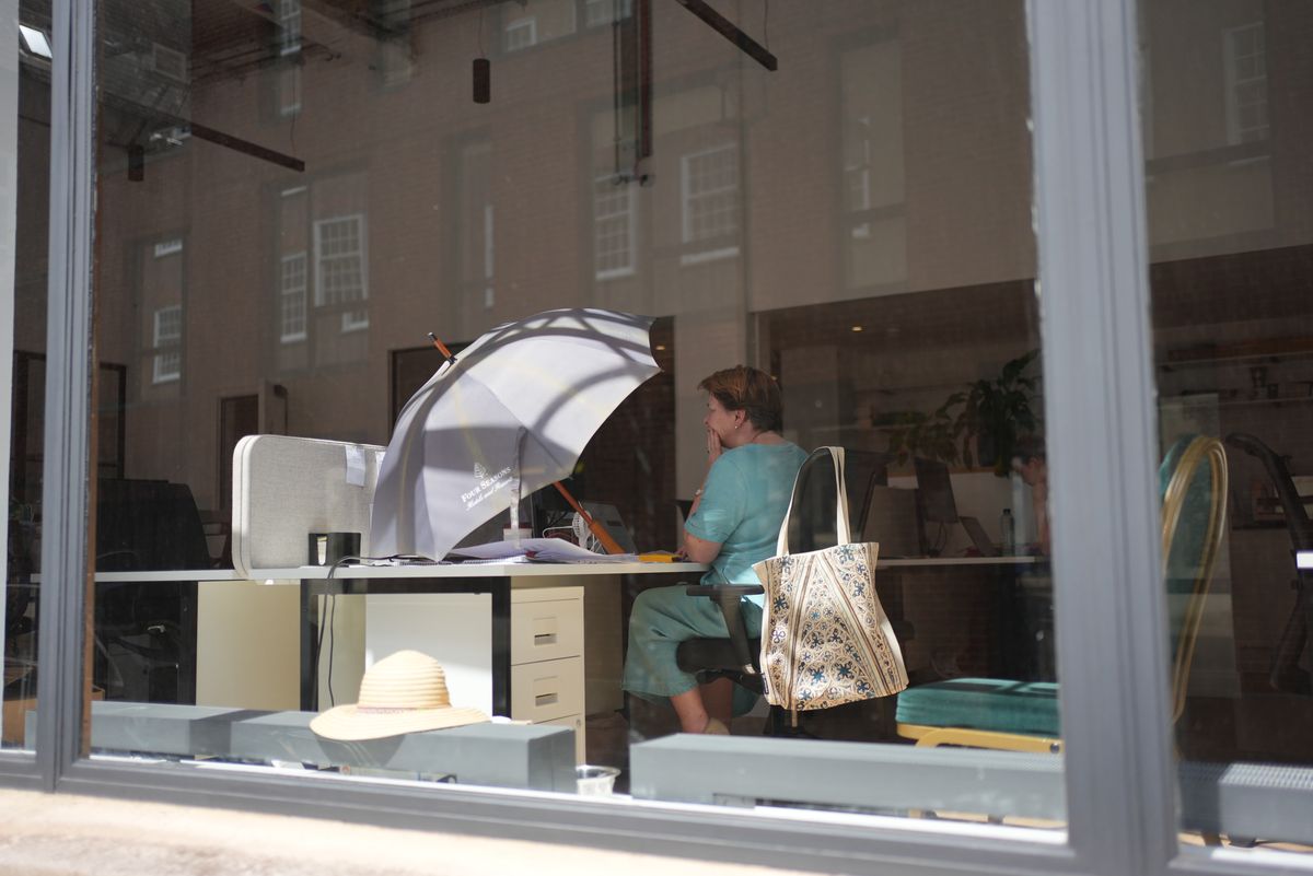 23/06/2026 - An office worker uses an umbrella to shade her workspace from the sun in Westminster, central London.