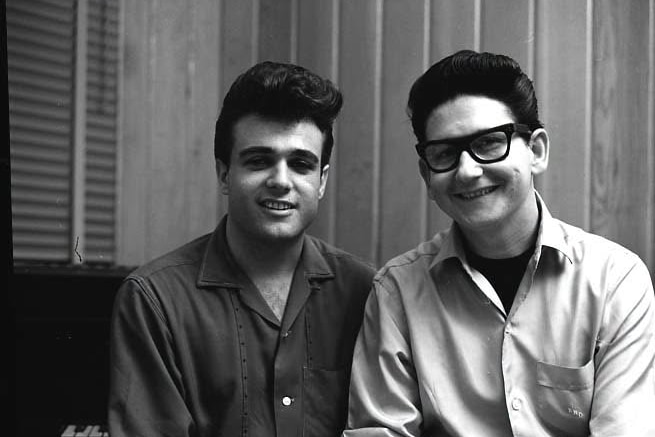 A black and white photo of Joe Melson and Roy Orbison sitting next to each other, smiling.