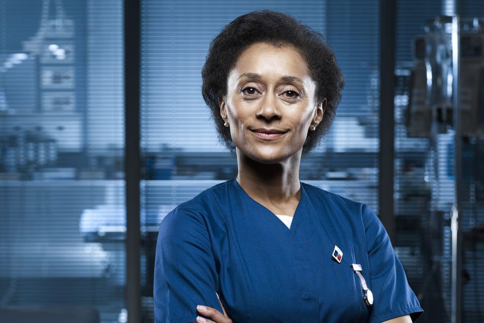 Tess in Casualty promo shot of tess in casualty, played by suzanne packer, wearing her blue uniform against a hospital background