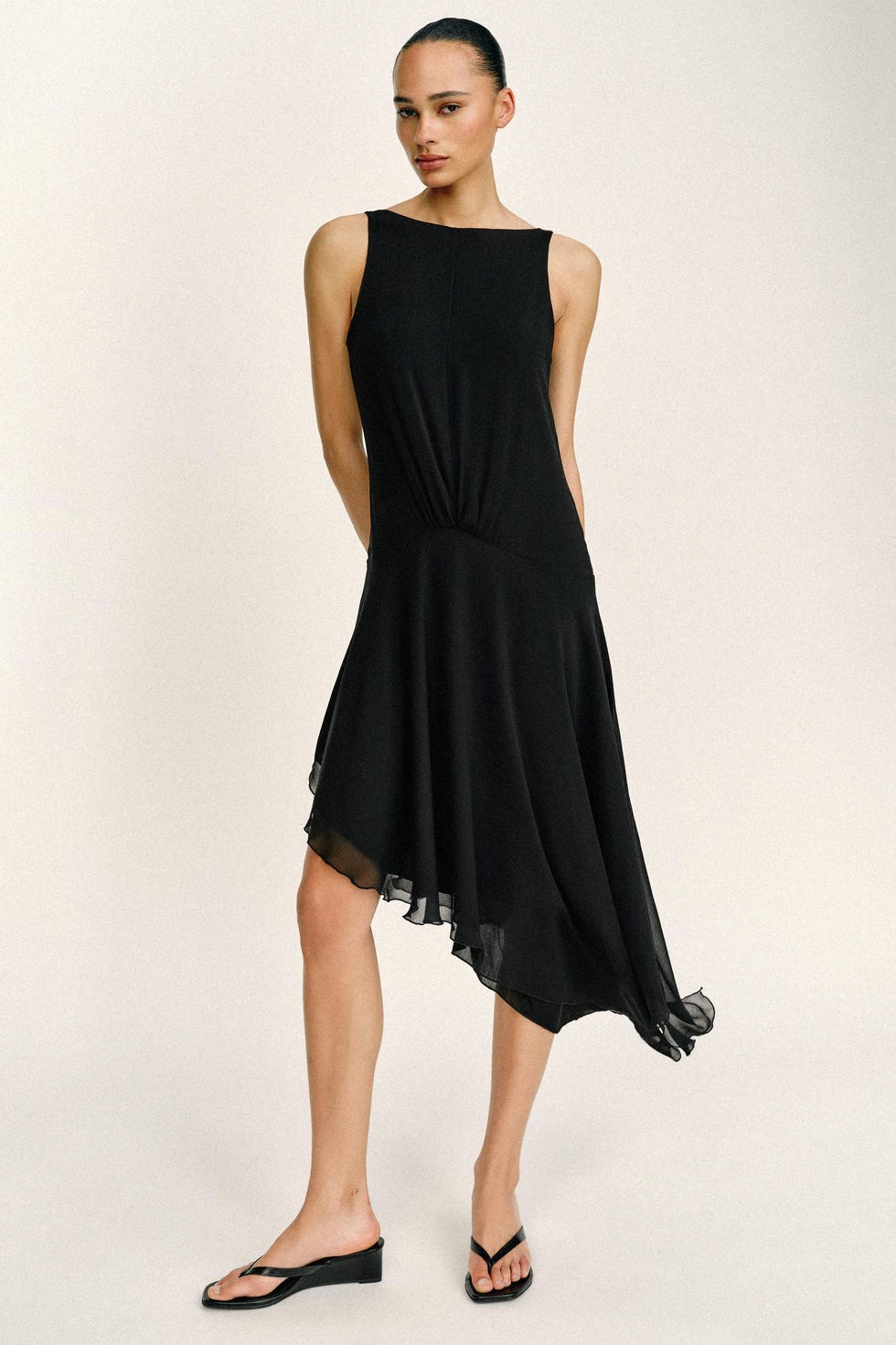 Woman wearing a black sleeveless asymmetrical dress and black sandals. woman wearing a black sleeveless asymmetrical dress and black sandals.
