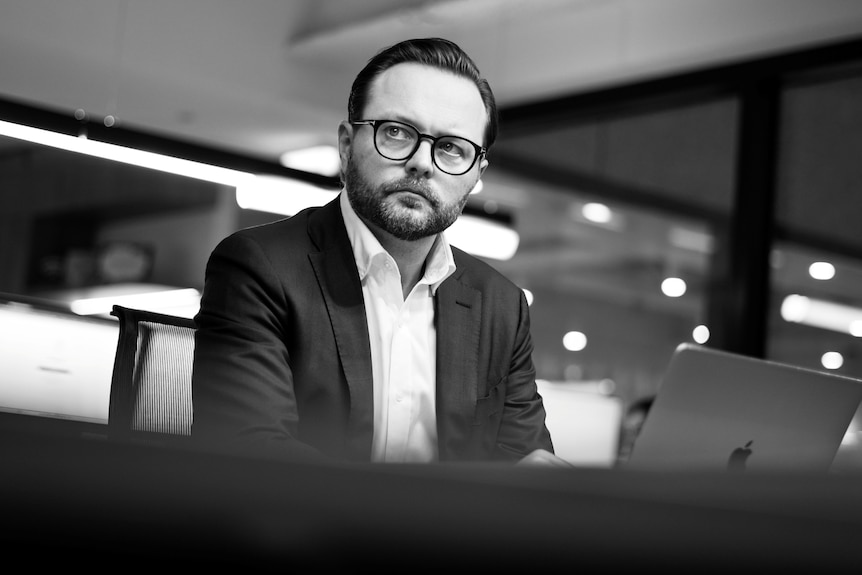 A man in glasses and a suit looks off camera