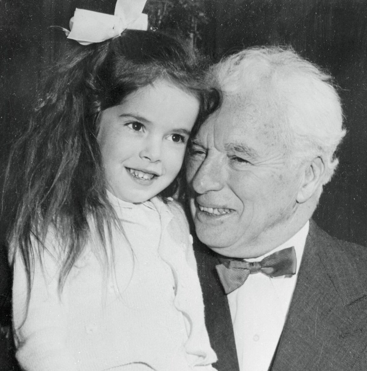 Just turned 65, filmdom's great comedian Charles Chaplin accepts a birthday hug from his daughter, Josephine. 