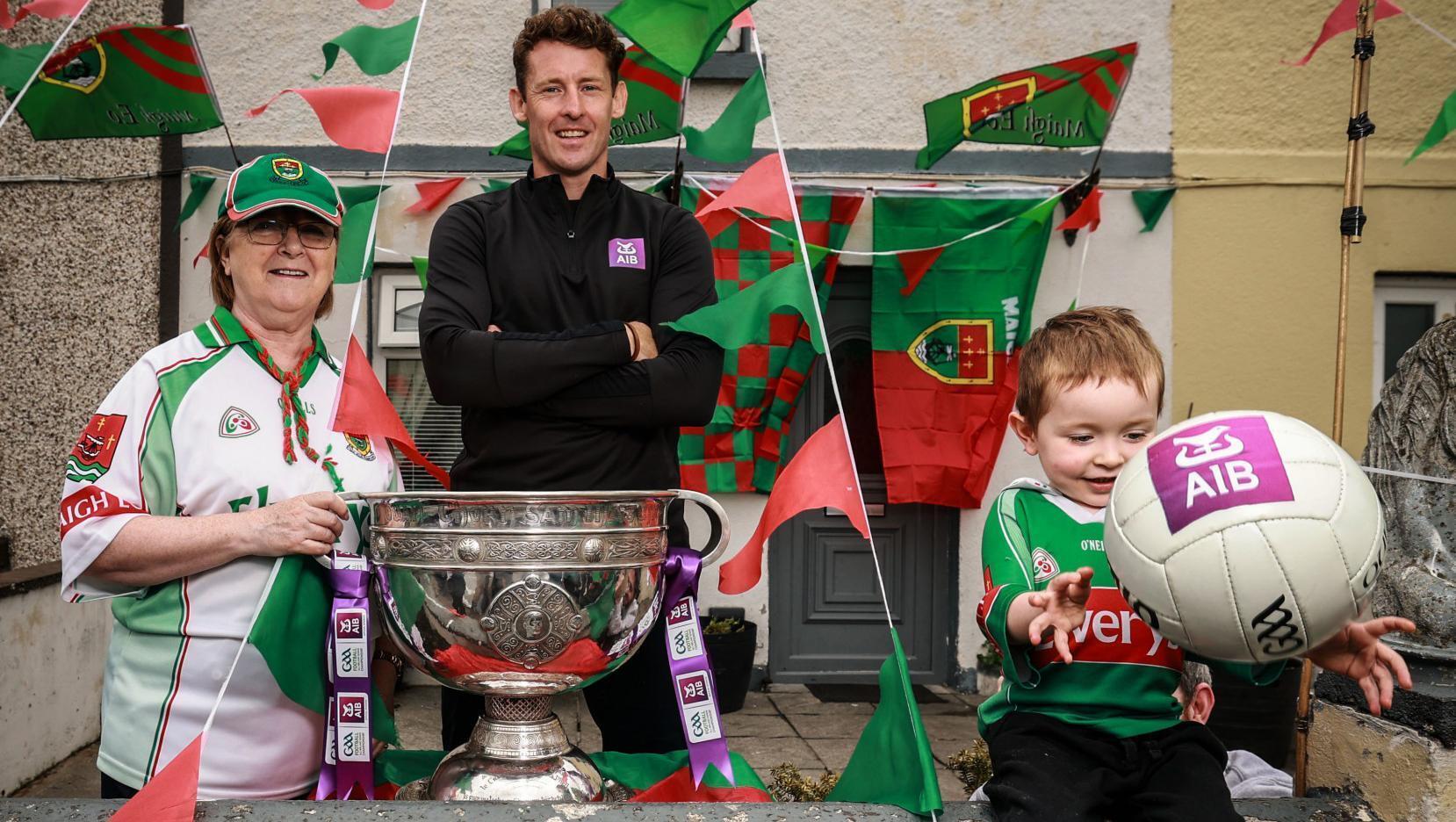 EARLY WARNING: Former Mayo Star David Clarke alongside Dorothy McDonnell and Matthew Carr, aged 4, pictured in Ballina for AIB ahead of the 2026 GAA All-Ireland Senior Football Championship Finals. Pic: ©INPHO/Dan Sheridan.