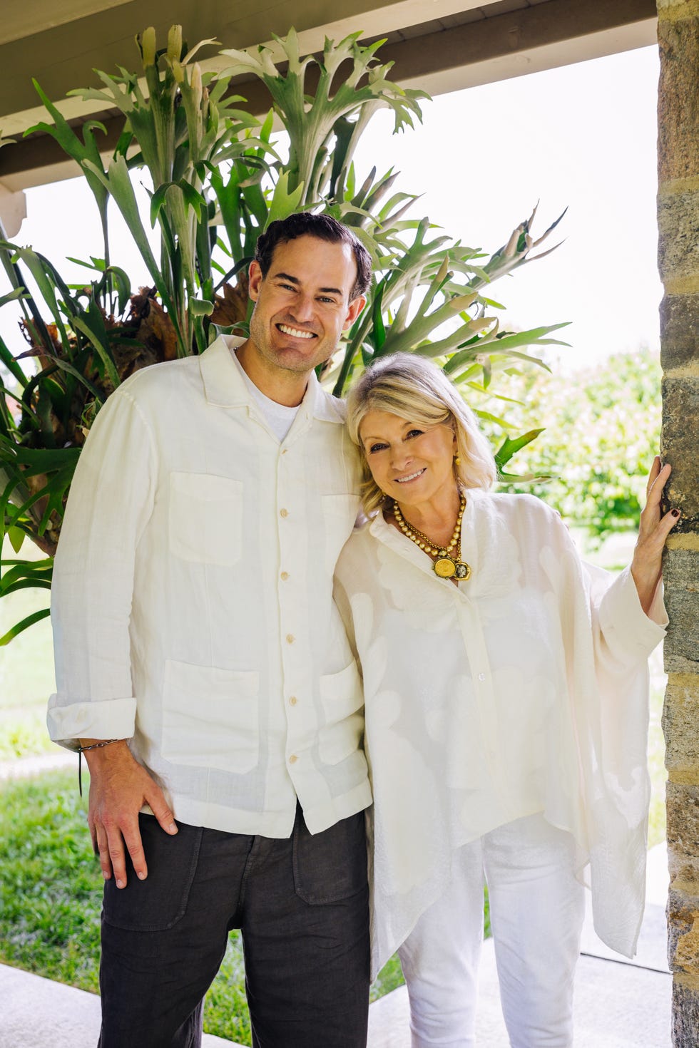 Two smiling people posing together outdoors with greenery in the background.