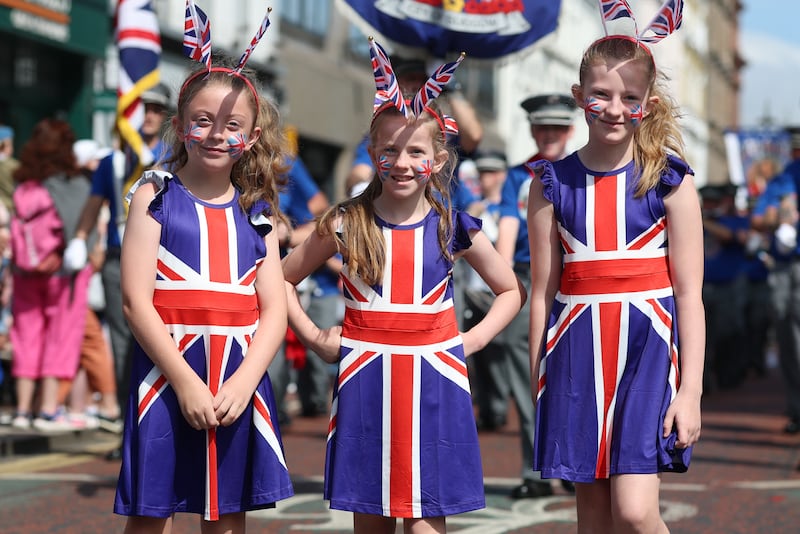 Ruby Bowes, nine, Holly McGilloway, nine, and Esme McGilloway, 10, from the Shankill, watch the Orange Order’s annual parade in Belfast. Photo: Liam McBurney/PA Wire