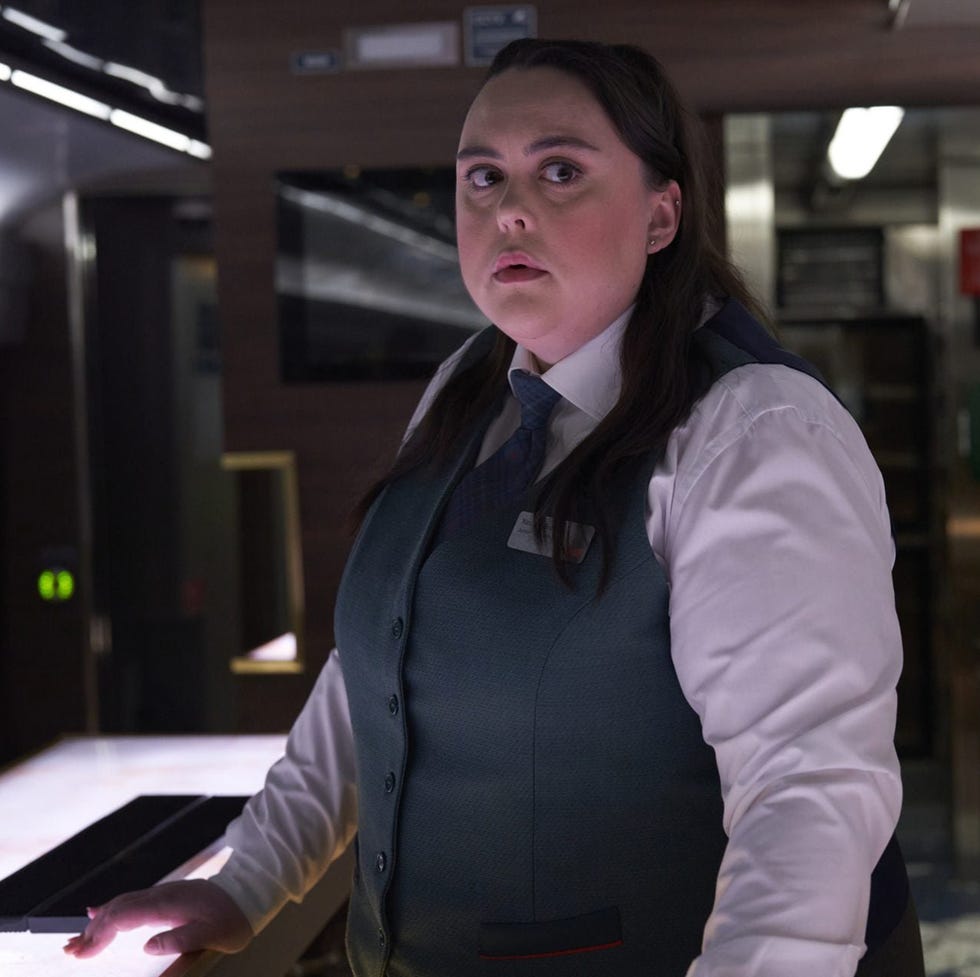 person wearing a uniform in a train's dining car looking towards the camera. person wearing a uniform in a train's dining car looking towards the camera.