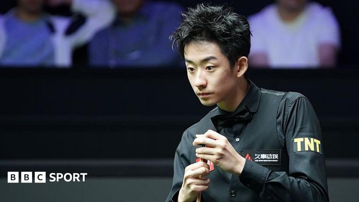 Wu Yize, wearing a black shirt and bowtie, chalks his cue with his left hand