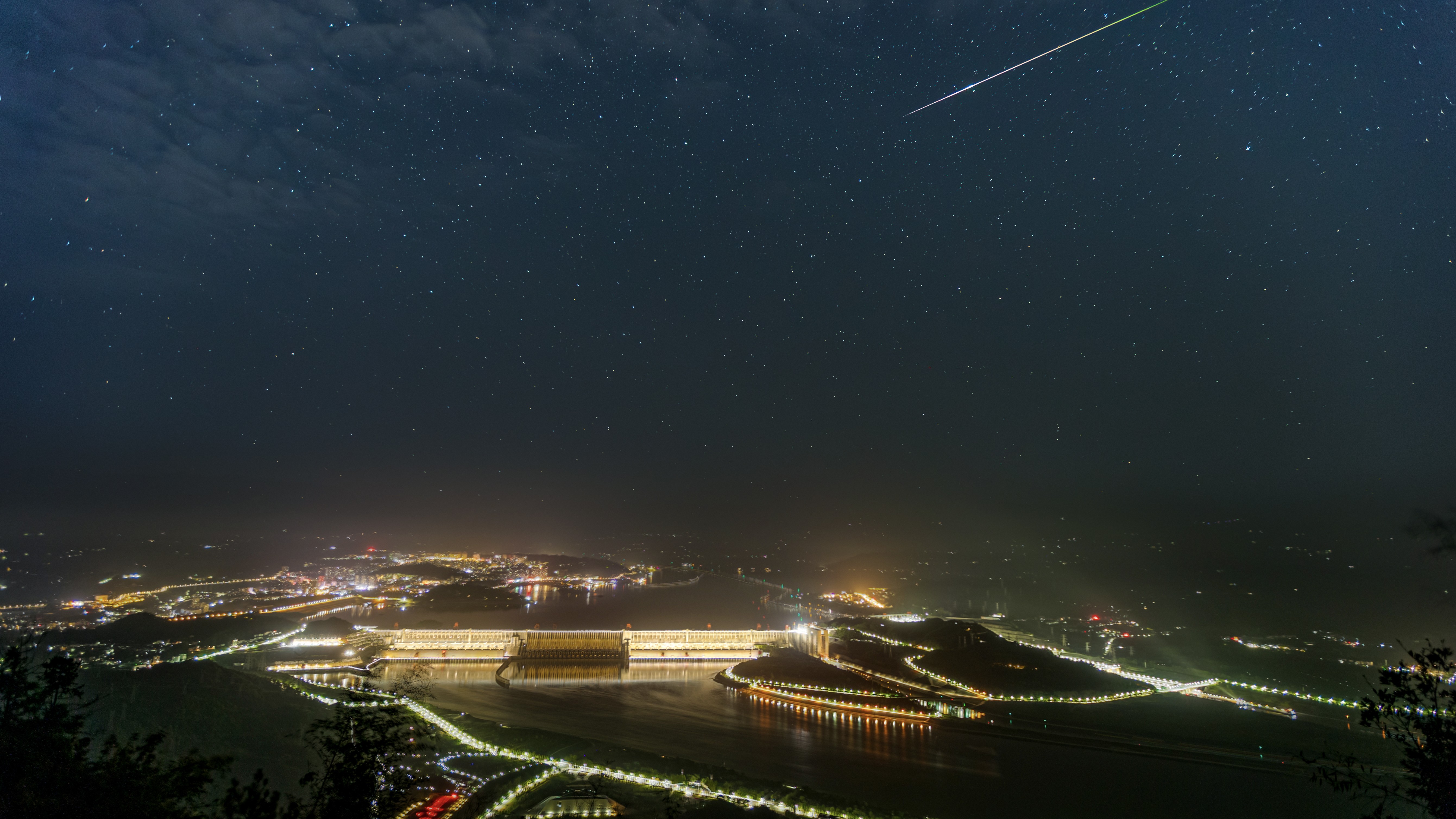 A meteor streaks earthward through a starry sky above an illuminated city.
