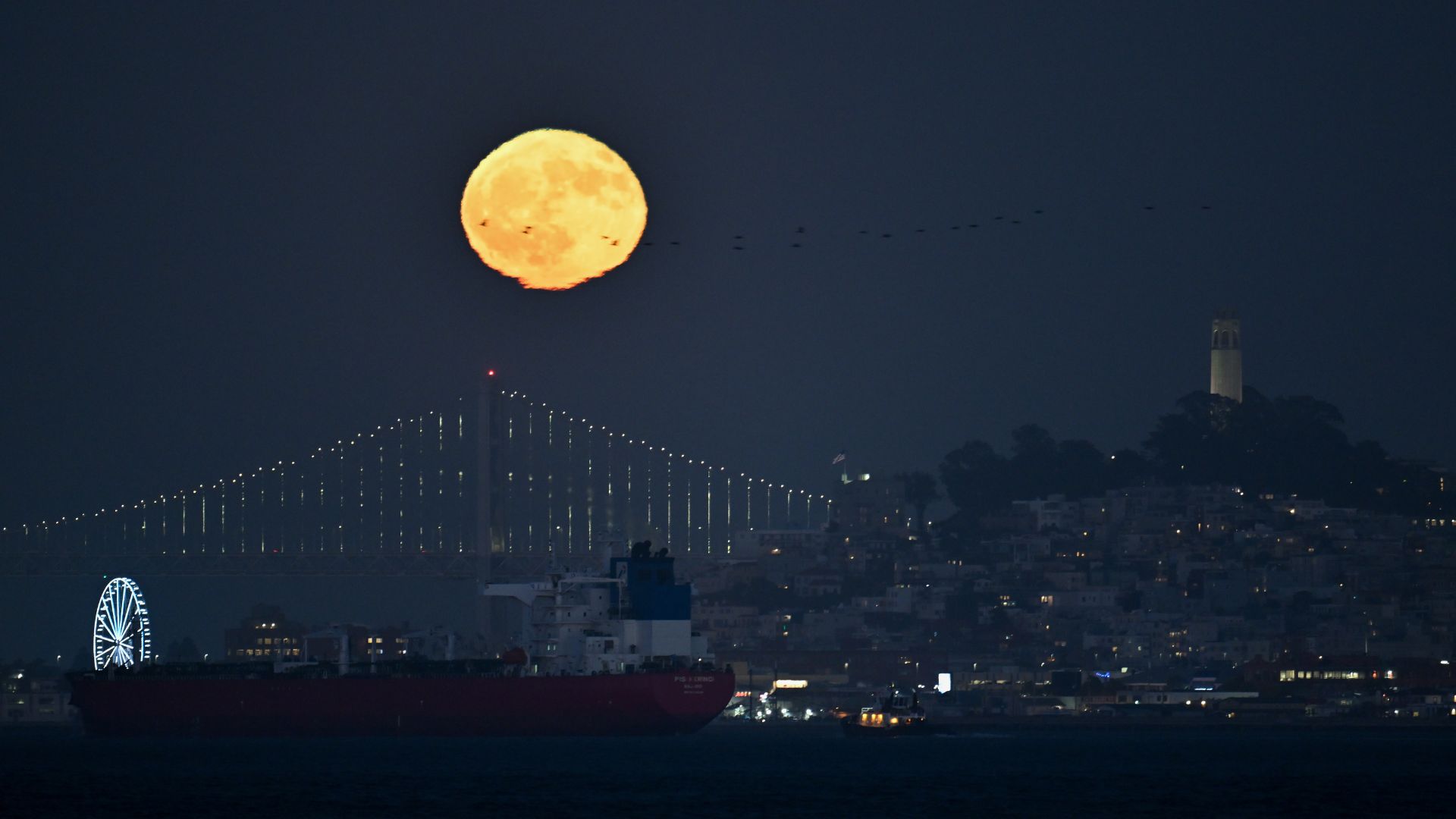 An orange moon glows over the Golden Gate Bridge in San Francisco at night.