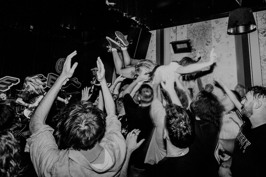 A person crowdsurfs at a live band performance.