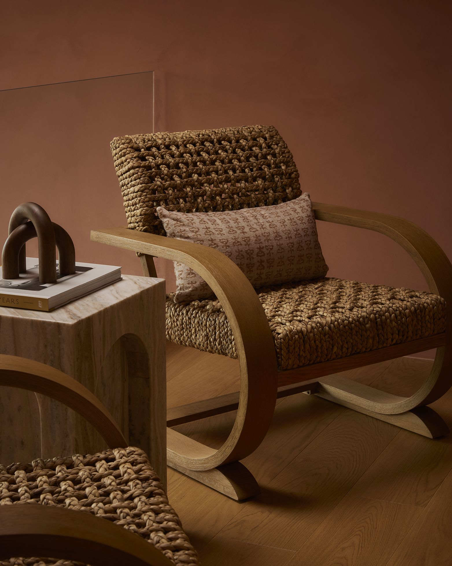 A terracotta living room with two matching wood and rattan sculptural armchairs, marble coffee tables, and unique collectibles.