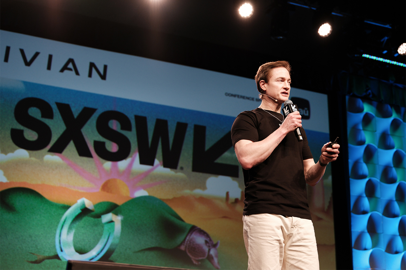 Bryan Johnson is standing on a stage and speaking into a microphone. He is wearing a black shirt.