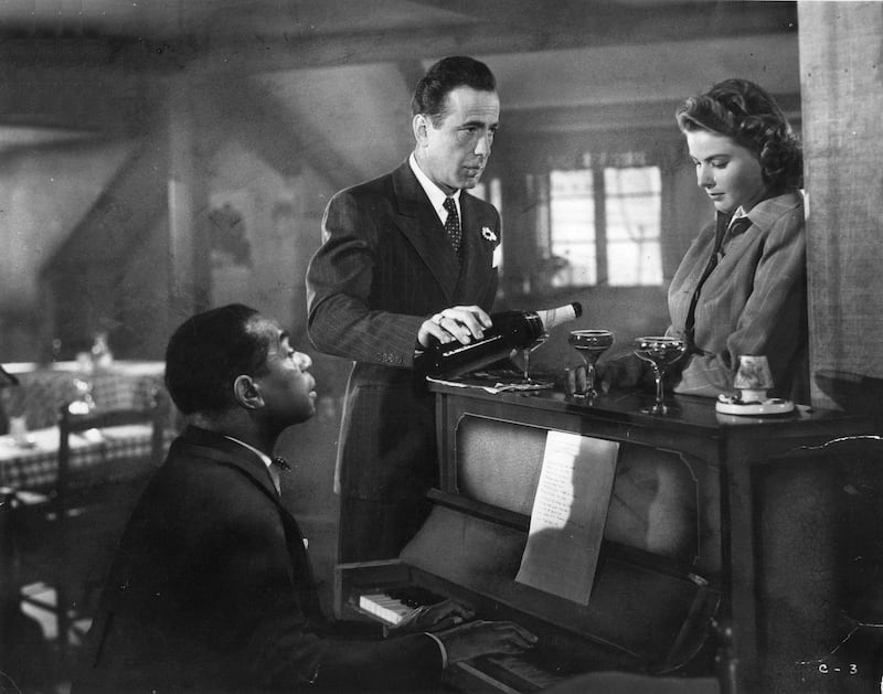 Dooley Wilson sits at the piano while Humphrey Bogart pours Ingrid Bergman a drink in a scene from the film 'Casablanca', 1942. (Photo by Warner Brothers/Getty Images)