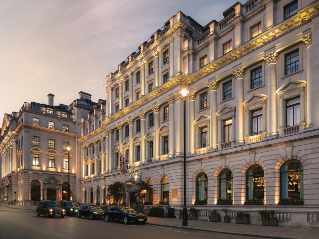The exterior of the Sofitel St. James hotel in Waterloo Place. It is a white Edwardian building, lit by lowlighting. Cars are lined up in front.