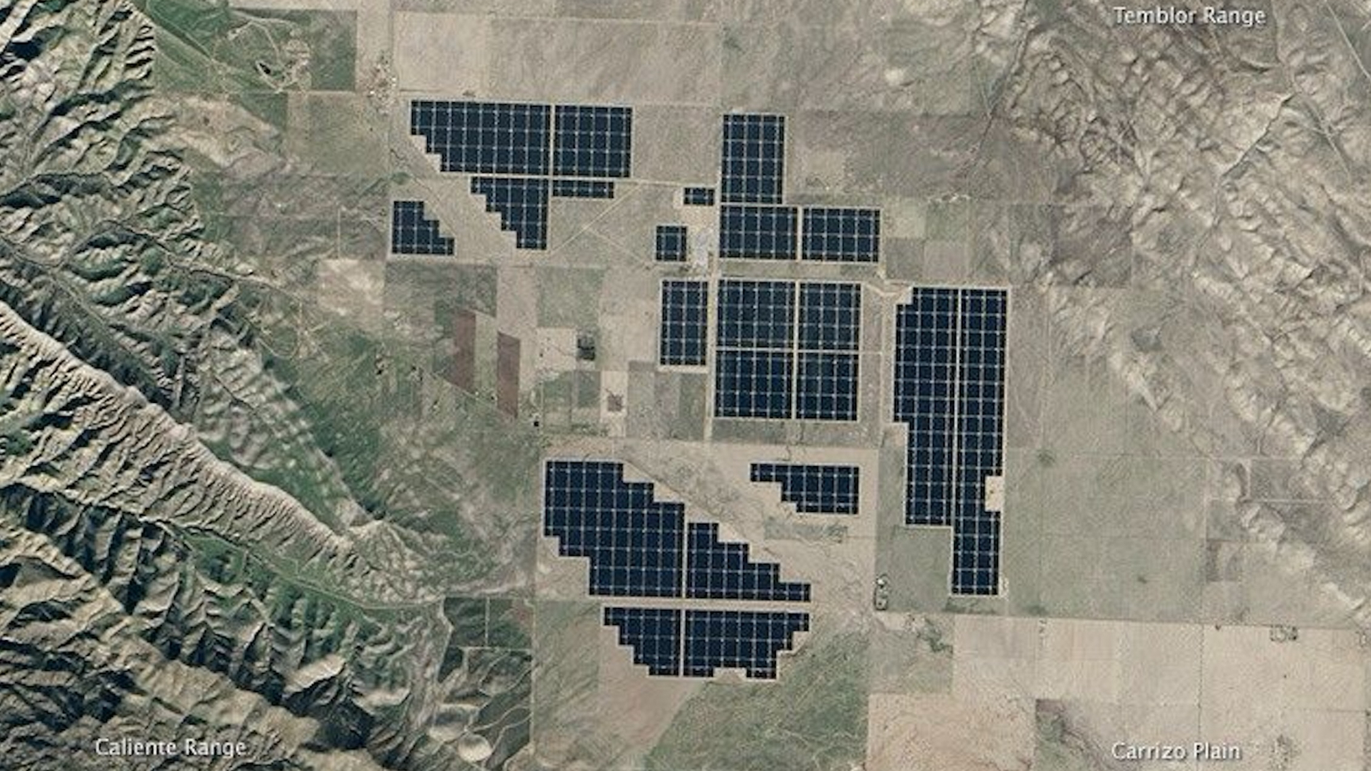 a large set of dark solar arrays in a desert landscape, seen from space