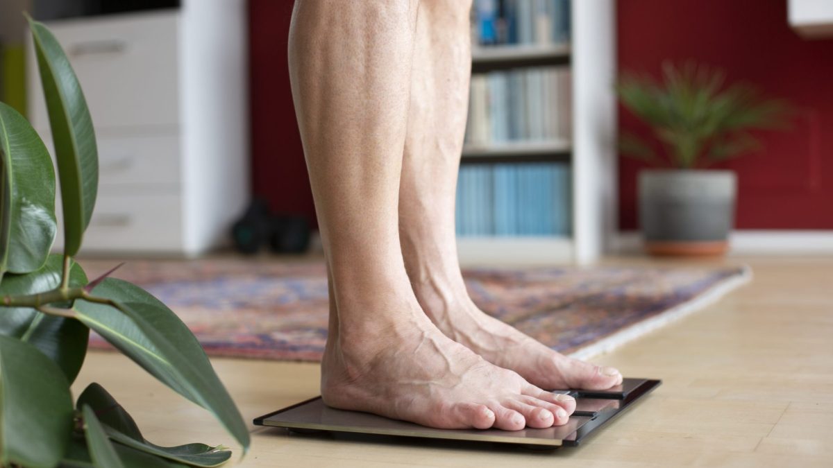 Man standing on weight scale, low section - stock photo