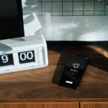 Smartphone on wooden cabinet rings at nine o'clock, next to digital flip clock at home interior. Sunbeam shining through the window on a fresh morning. A brand new day, fresh start, fresh energy, new opportunities. Waking up early for a healthy lifestyle - stock photo