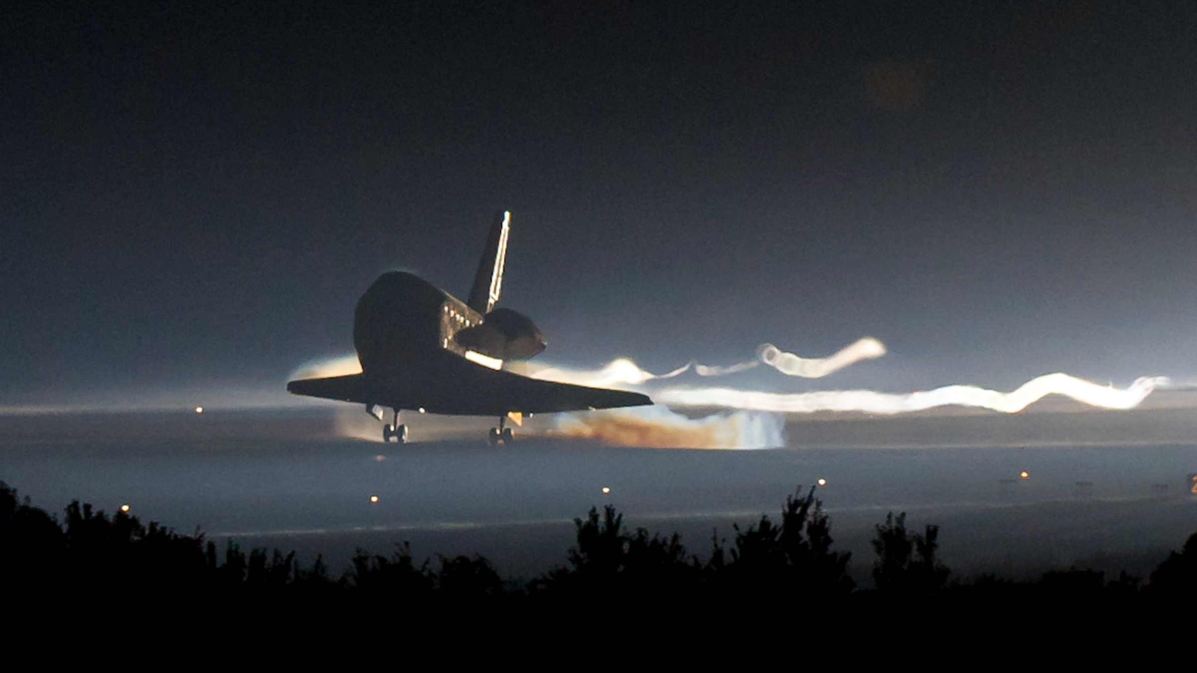 Photo of Atlantis touching down for the final time on a runway at the Kennedy Space Center at night