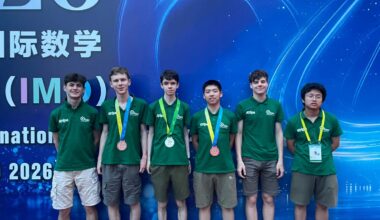 Six racially diverse teenage boys in Green shirts, showcasing bronze and silver medals, in front of a blue background.