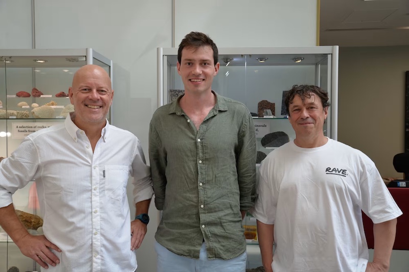 3 men standing in a lab. The middle man is the tallest.