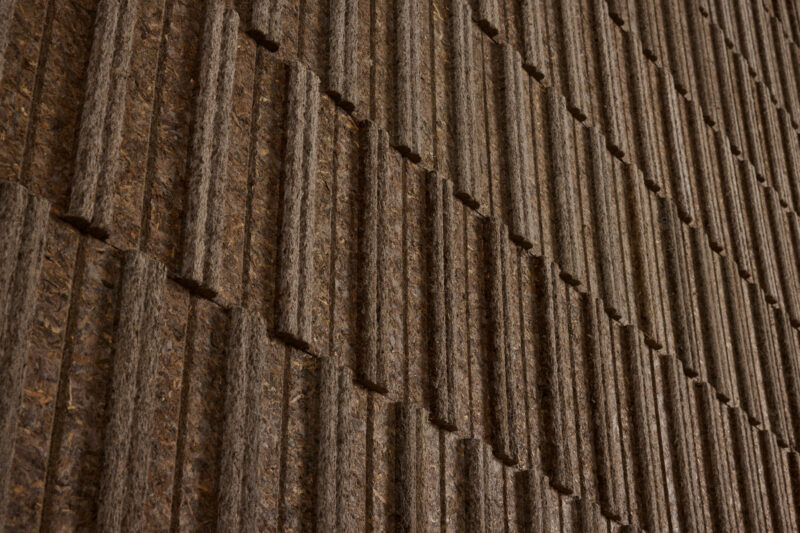 Close-up of a textured brown wall with evenly spaced vertical and horizontal ridges forming a repeating geometric pattern.