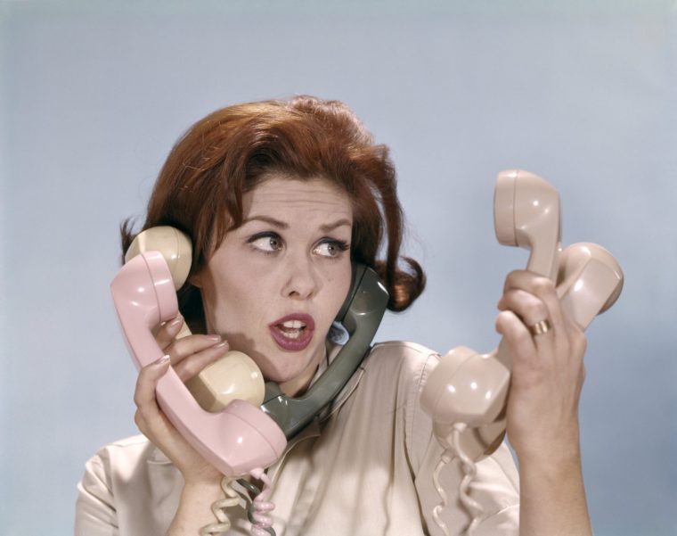 1960s FRUSTRATED YOUNG REDHEADED WOMAN TRYING TO ANSWER HANDLE FIVE TELEPHONE RECEIVERS STUDIO (Photo by H. Armstrong Roberts/ClassicStock/Getty Images)