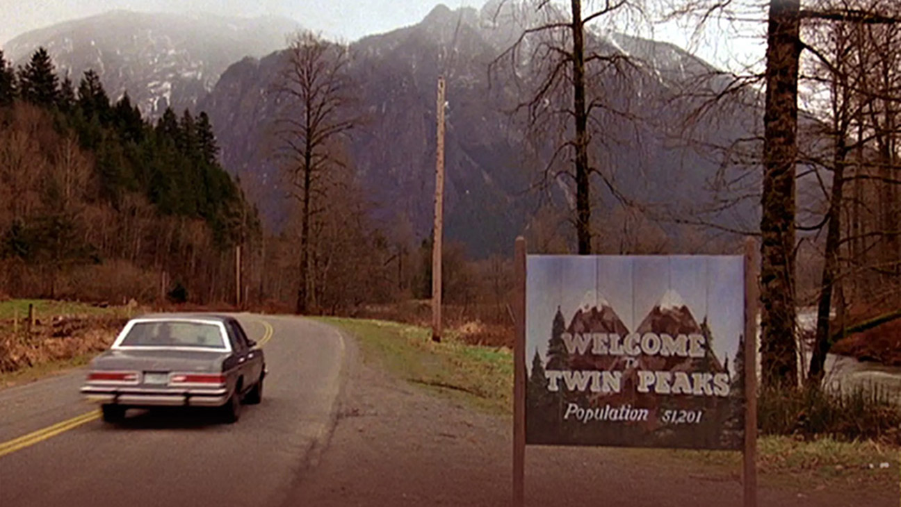 An image from the 1990 television series ‘Twin Peaks’ showing a car passing a sign that says “Welcome to Twin Peaks.”
