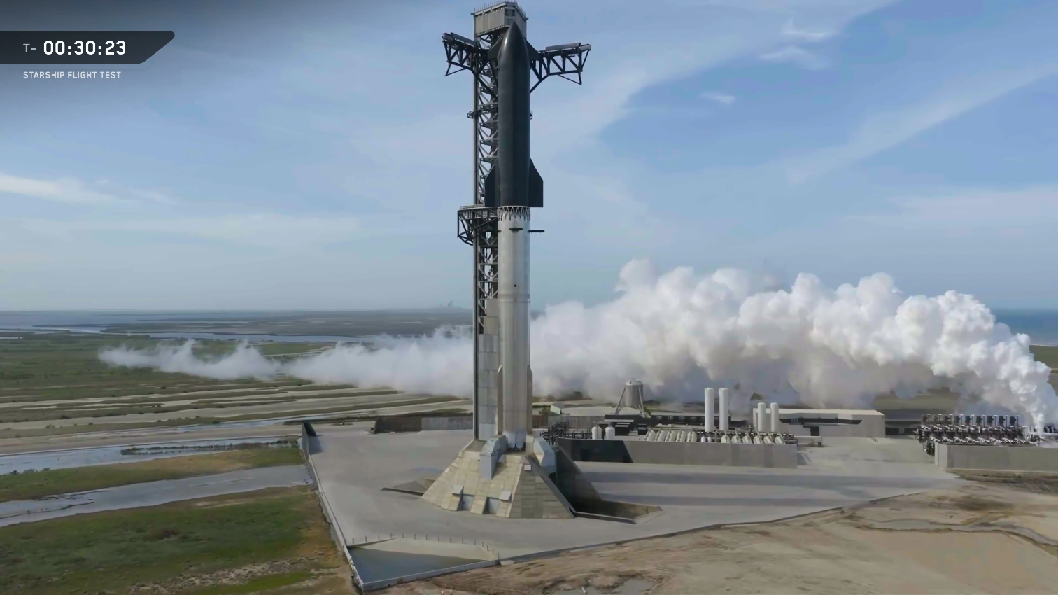 A giant steel rocket stands next to a launch tower against a cloudy sky