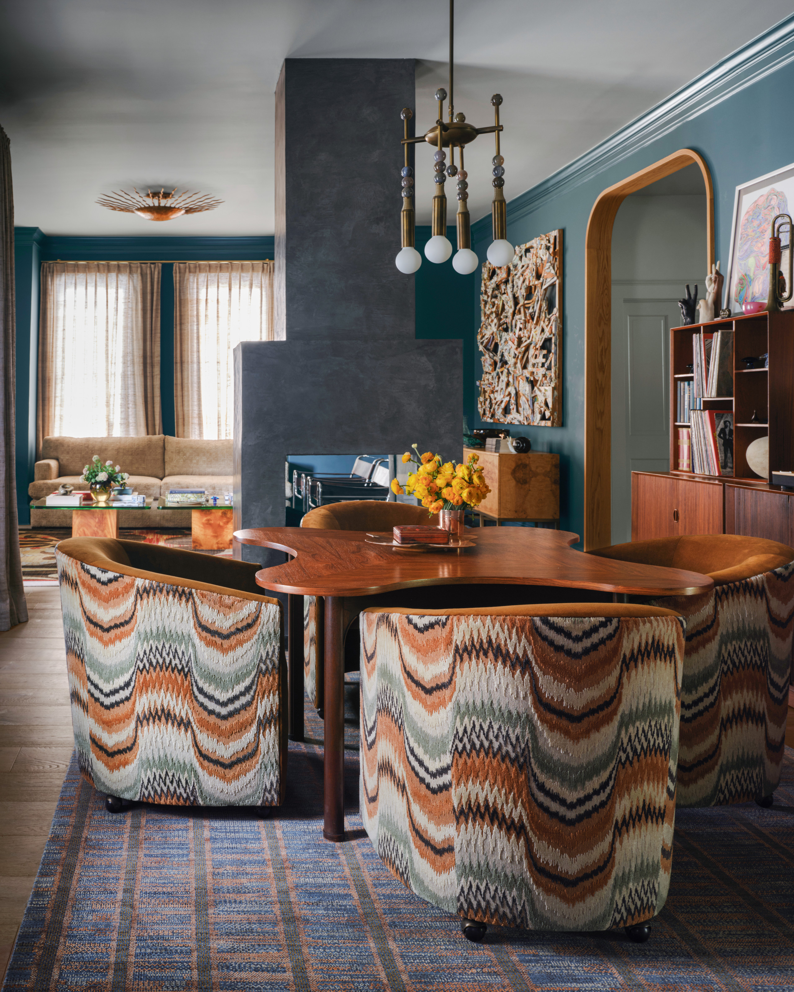 Dining area with curved wood table, blue, white and brown patterned armchairs, blue walls and blue gridded rug