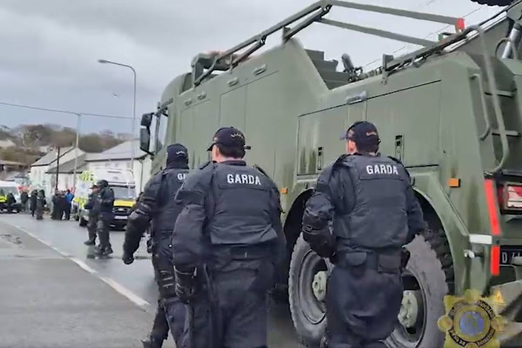 Garda officers walking beside a Defence Forces vehicle at Whitegate Marine Terminal