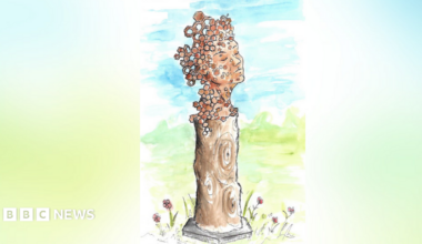 A statue which features a woman's face looking up calmly while on a wooden plinth.