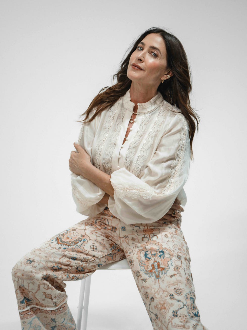 Person seated wearing a white blouse and patterned pants.