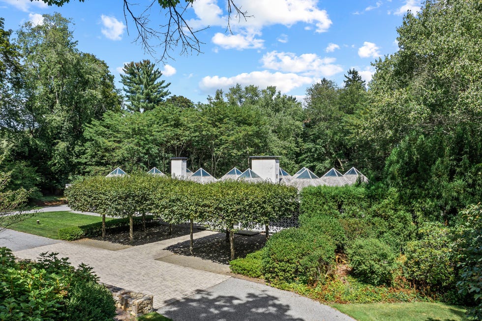 Lush green garden with a path and modern structures under a blue sky dotted with clouds.