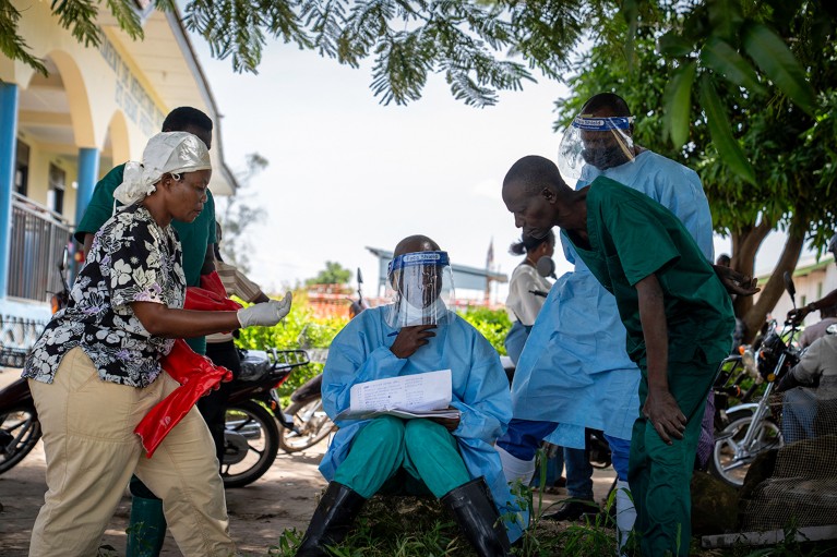A seated health worker wearing PPE, shows his colleagues the list of patients at Rwampara Hospital in Ituri, in the eastern Democratic Republic of the Congo.