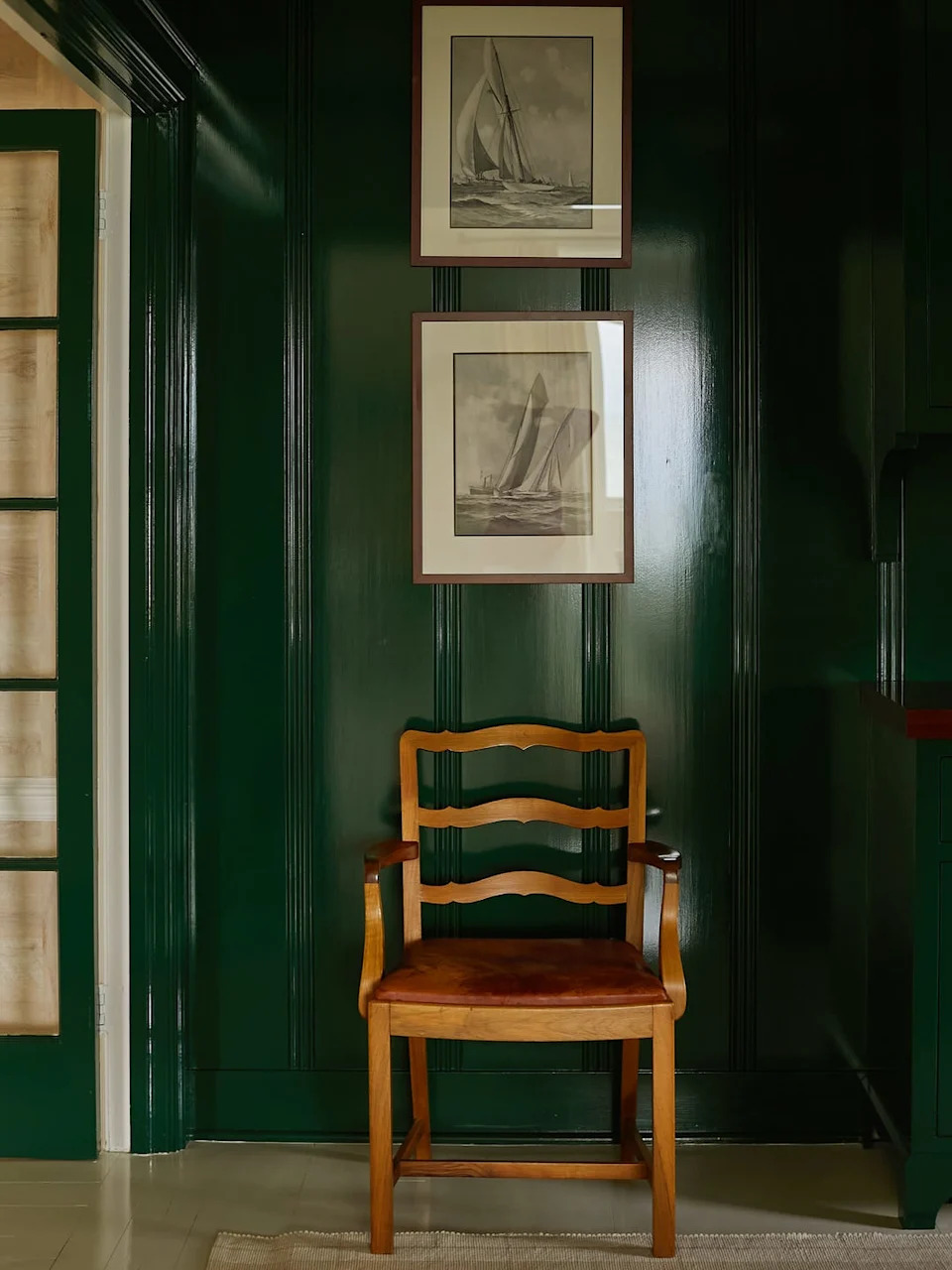Wooden chair in front of a green wall with two framed nautical prints.