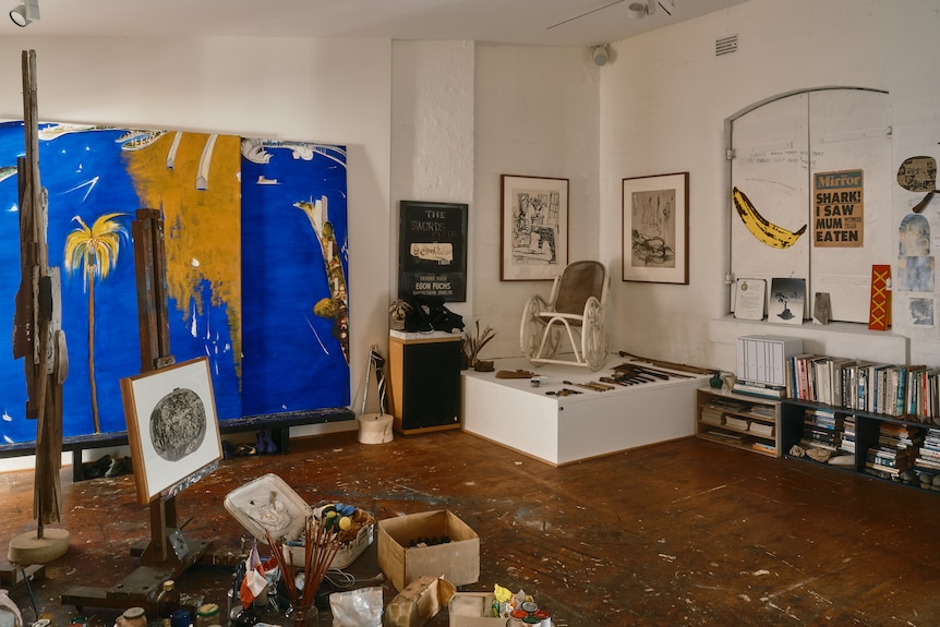 Brett Whiteley's studio space, including a half-finished ultramarine blue landscape painting and cups and boxes of paint.