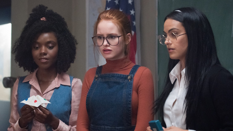 Ashleigh Murray as Sierra McCoy, Madelaine Petsch as Penelope Blossom, and Camila Mendes as Hermione Gomez, all wearing '80s-inspired outfits and starring at something in disbelief in "Riverdale."