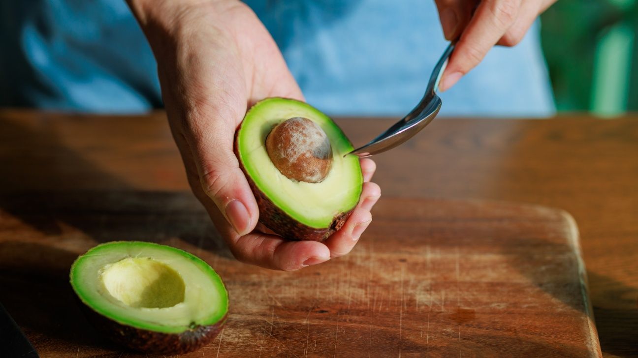 Female hands peeling an avocado with a spoon