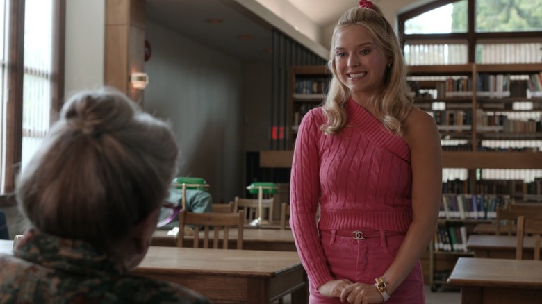 Elle smiling in front of a teacher at her desk in a pink outfit