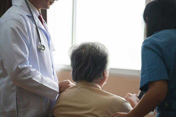 Hospital employees, a doctor and nurse, assisting an elderly patient in a wheelchair, illustrating hospital stories.