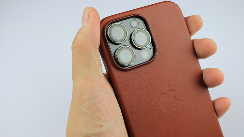 A person's hand holding an Apple-branded leather case for the iPhone.