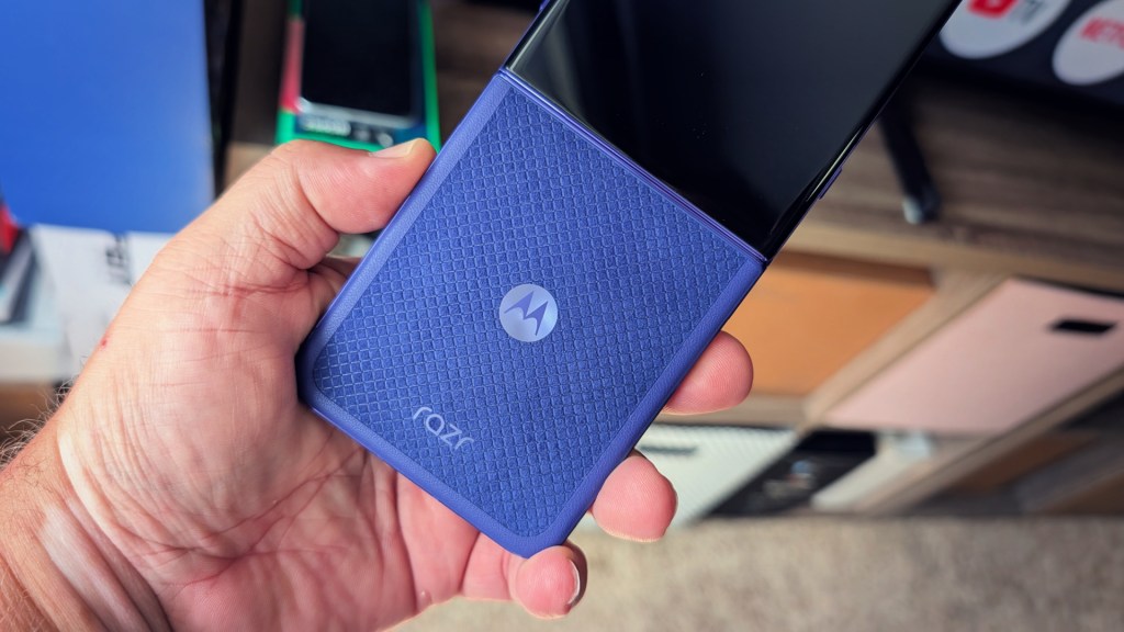 A person holding a Motorola Razr smartphone featuring a blue textured back design, with the screen facing upwards.