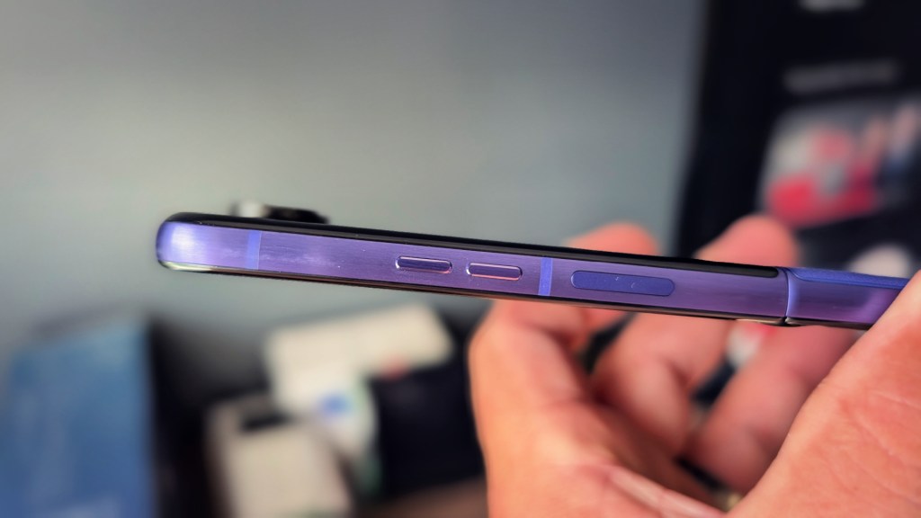 Close-up of a person's hand holding a smartphone, showcasing the side buttons and purple color of the device.