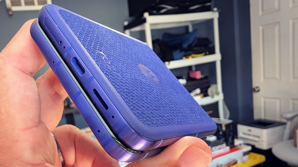 A person holding a purple device with a textured surface, showcasing various ports on the side, with a blurred background of shelves and items.