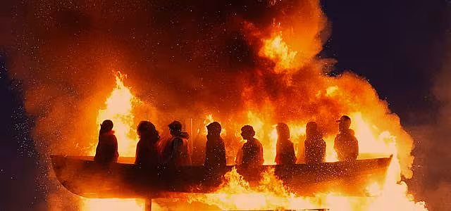 Effigies of migrants in a boat burning on a bonfire