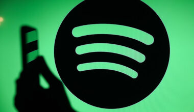 The Spotify logo displays on a screen with a person holding a phone.